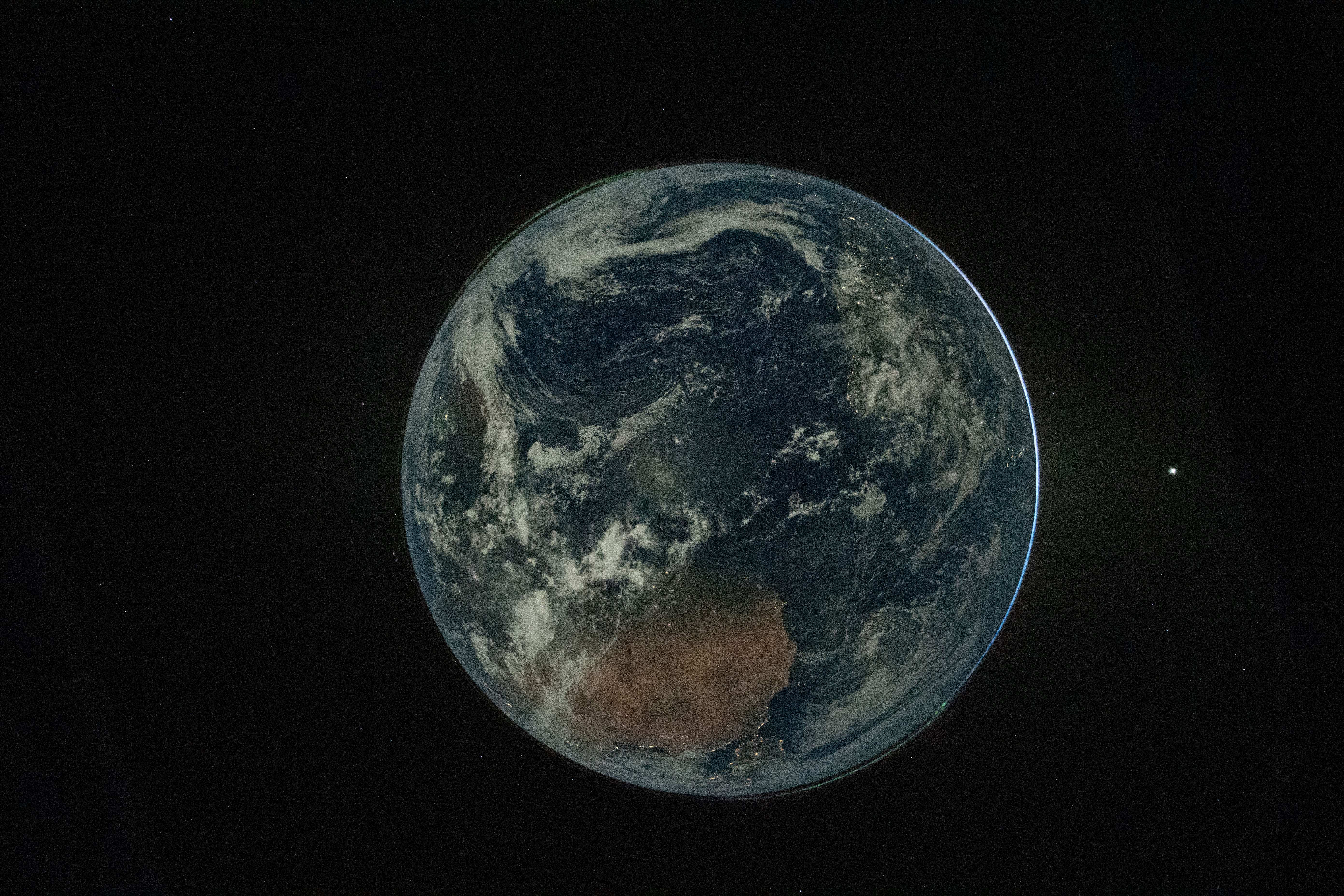 A nearly full-disk view of Earth against a black star field, with Australia prominent beneath the moonlit Pacific.